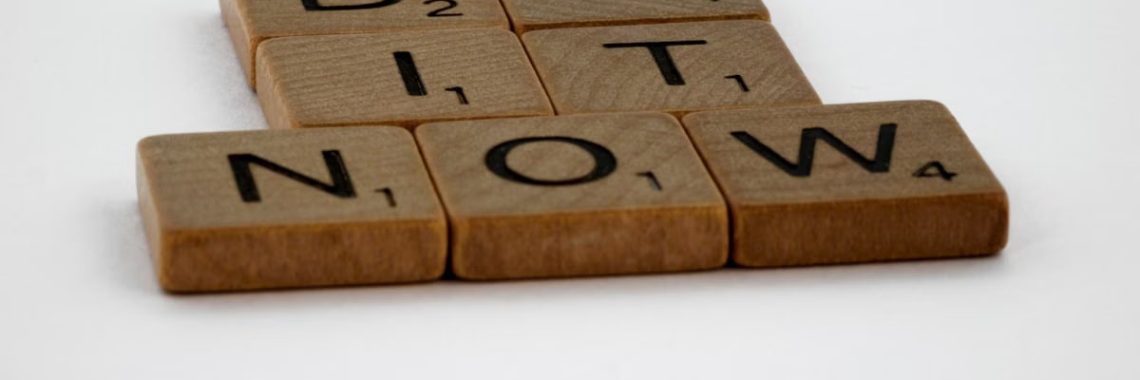 Wooden Scrabble tiles spelling 'Do It Now' on a white background. Motivational concept.